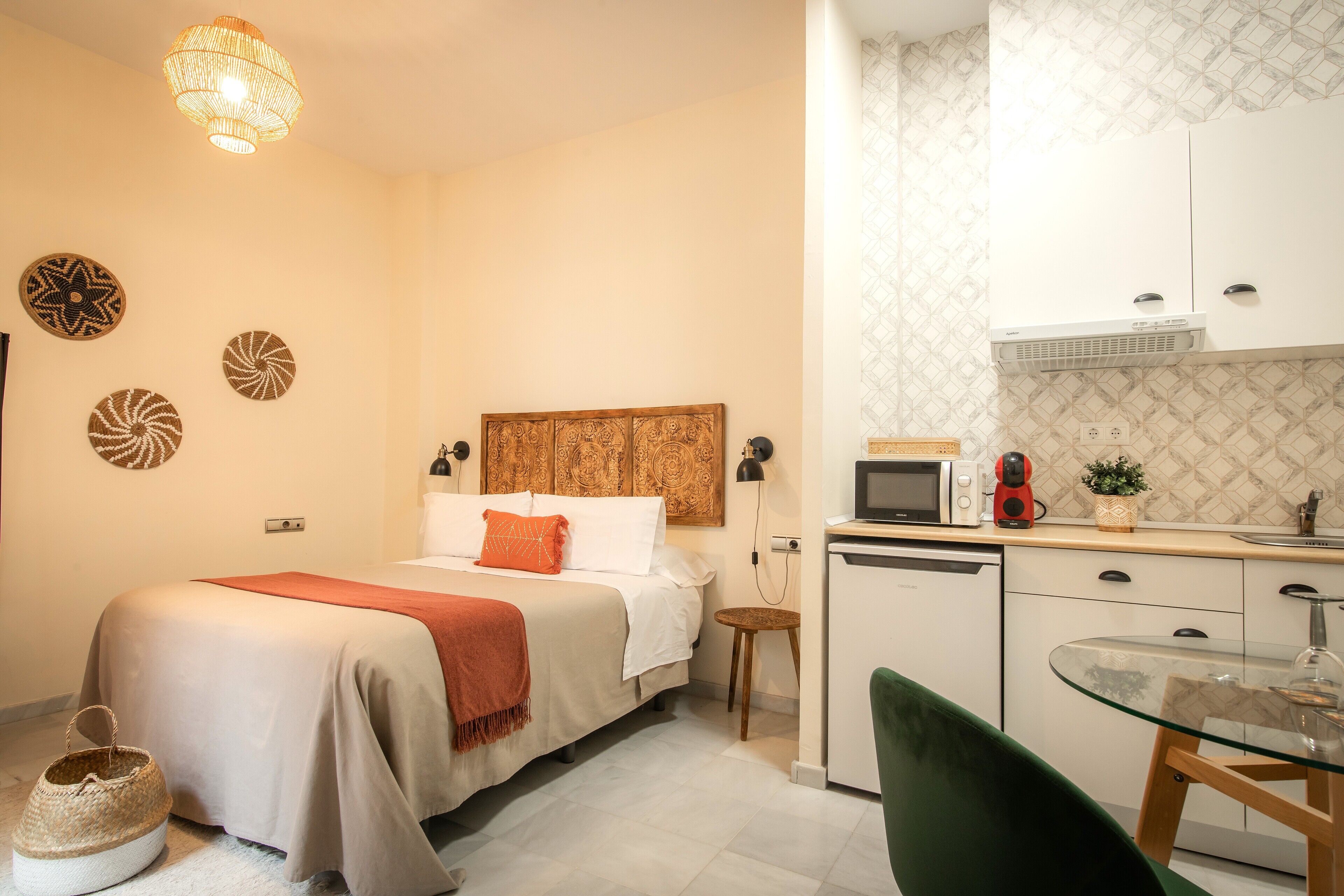 Een compacte hotelkamer met een bed, nachtkastje en een kleine kitchenette.