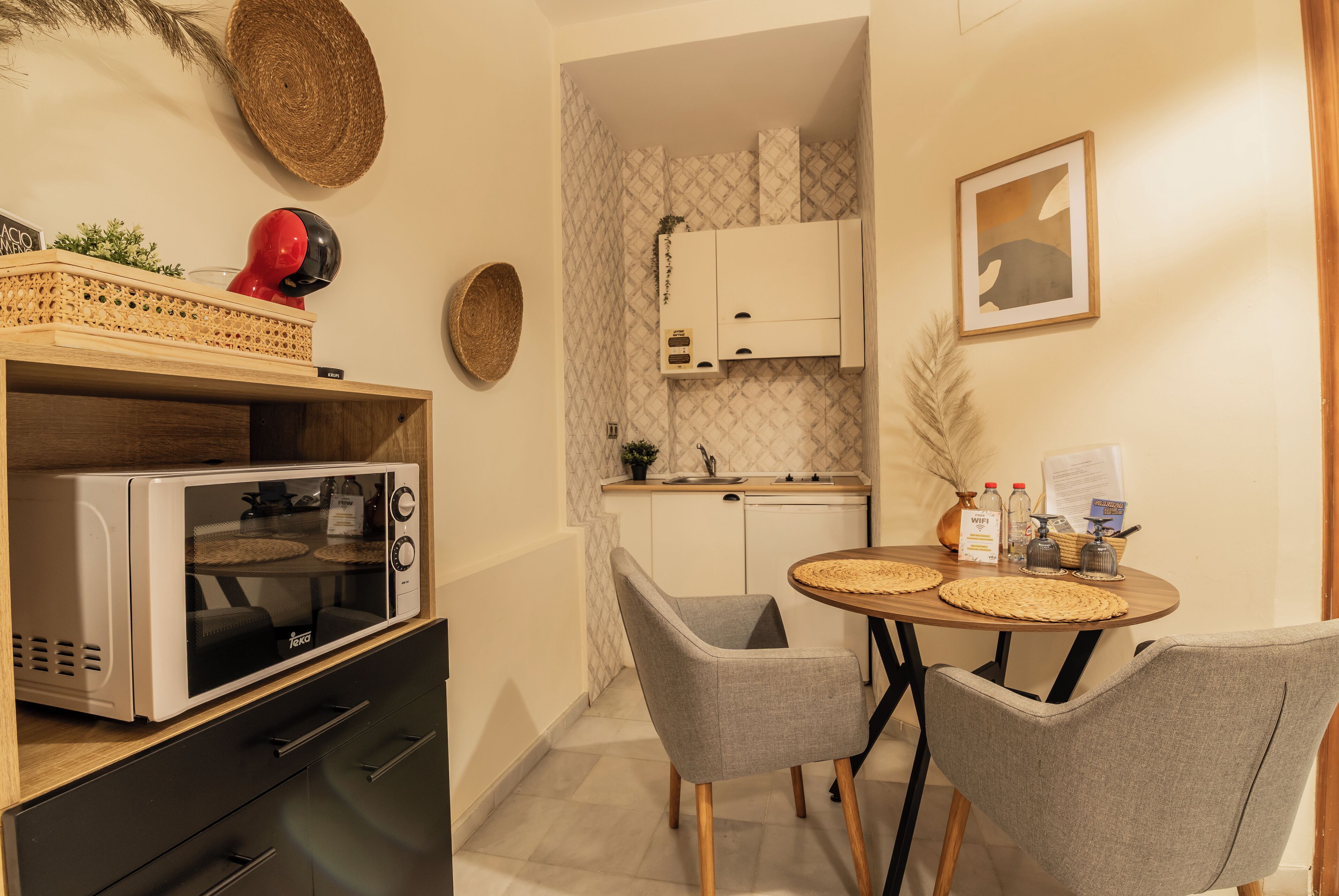 Una cocina compacta con microondas, una pequeña mesa de comedor con sillas y un armario.