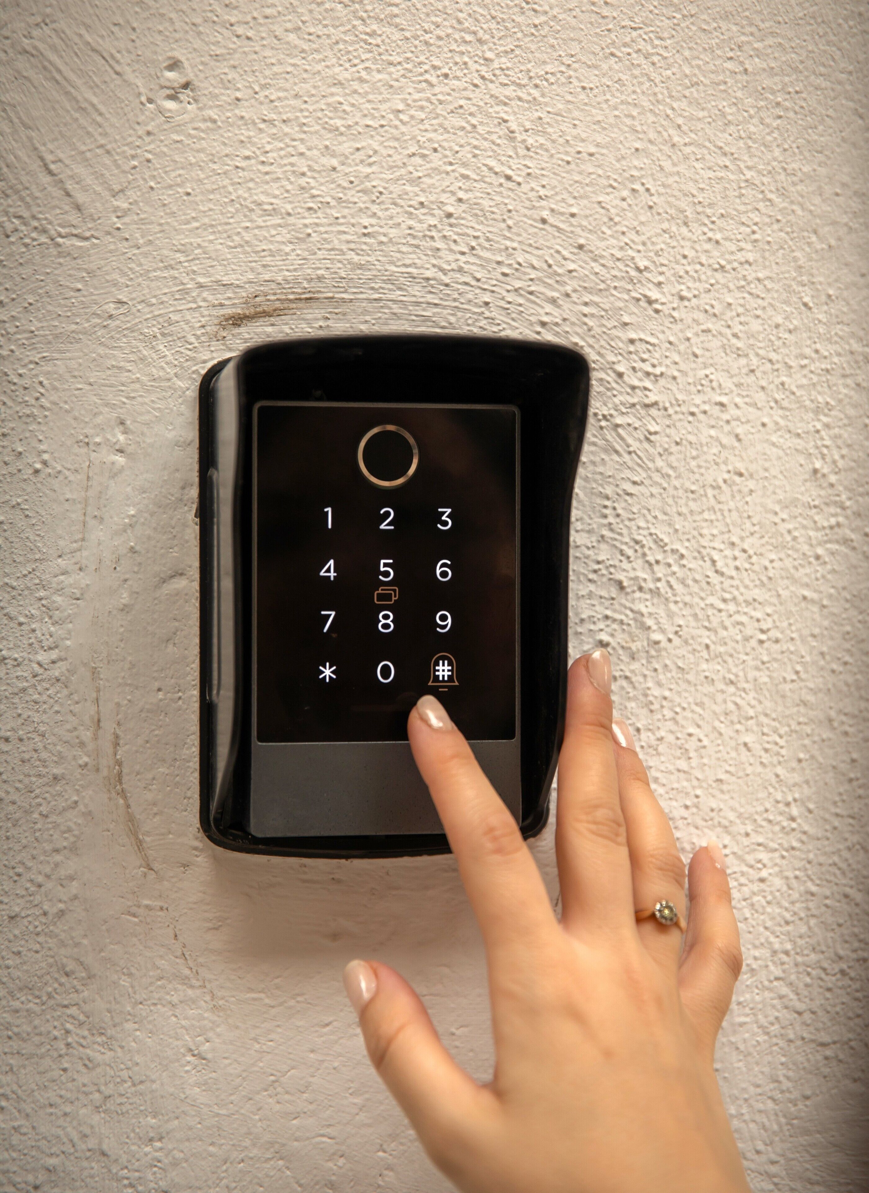 A keypad on a textured wall, with a hand pressing a button.