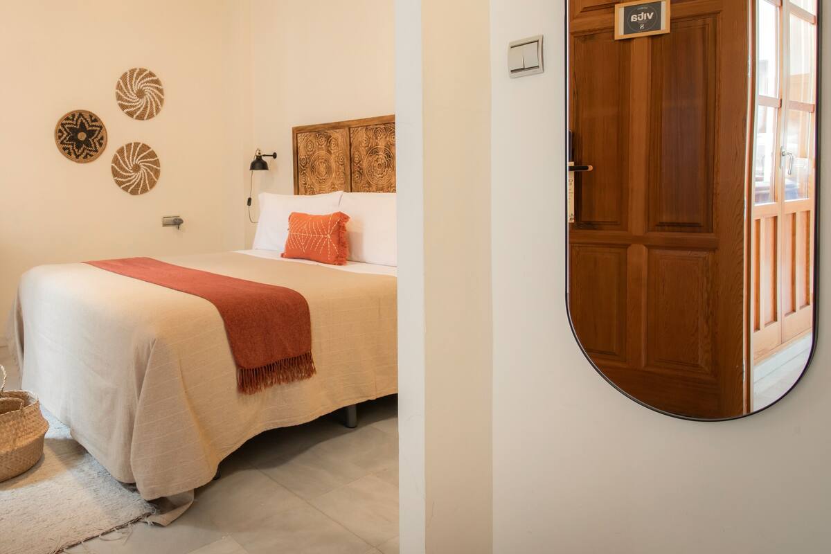 A bedroom with a bed, a wooden door, and a mirror on the wall.