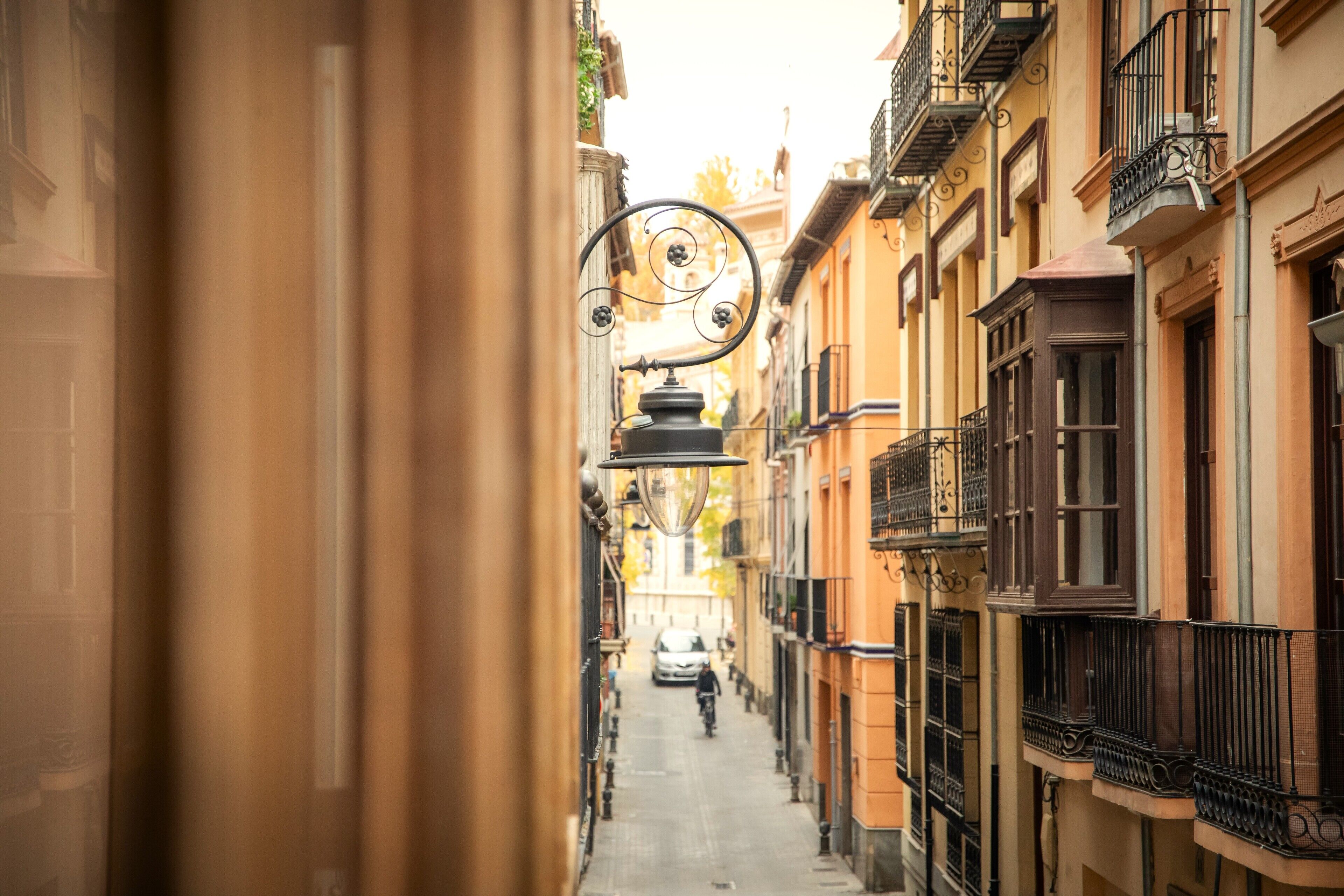 A narrow street with buildings on either side, a street lamp, and a person walking in the distance.
