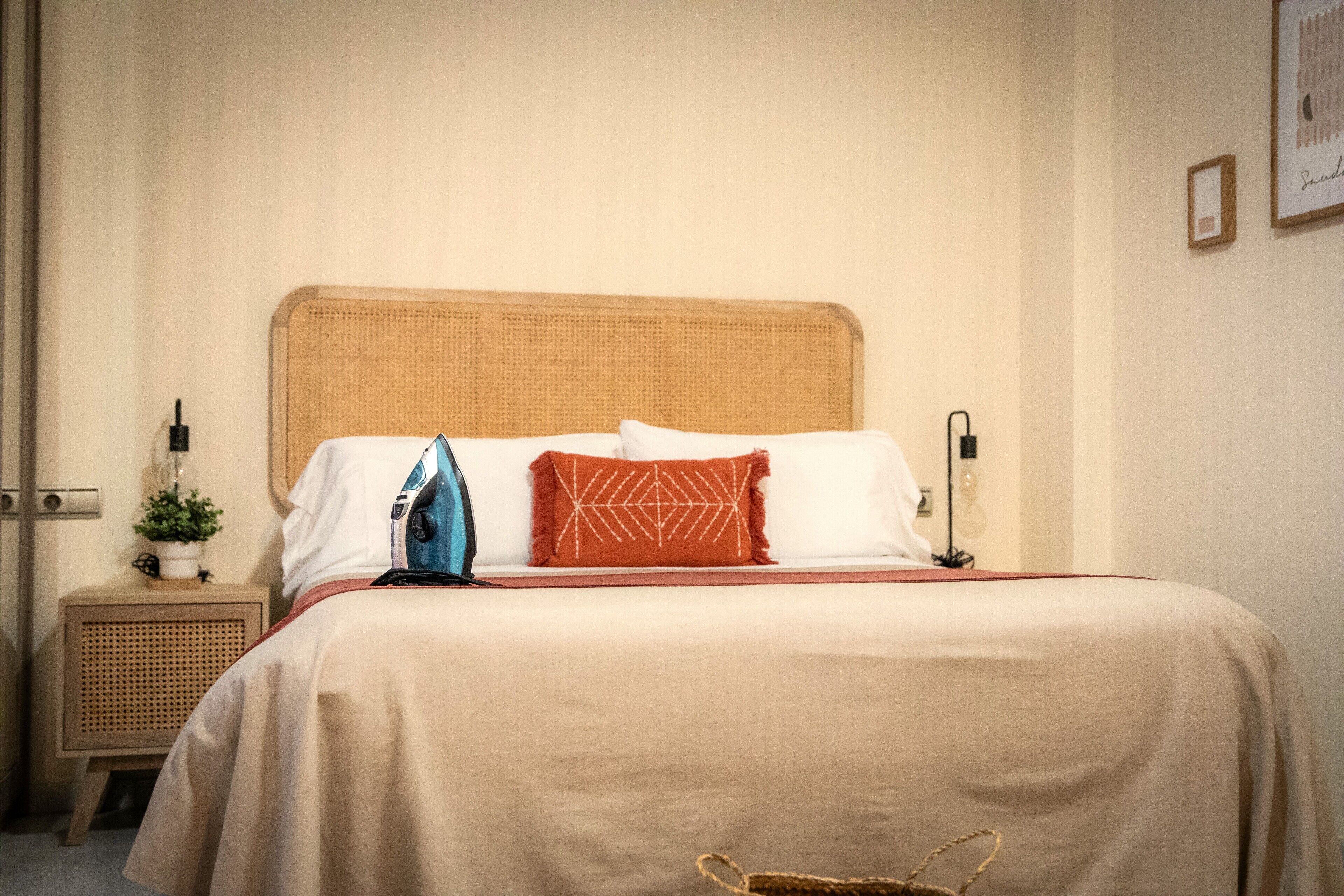 Una cama bien tendida con una colcha color beige, un planchado azul y dos almohadas decorativas.