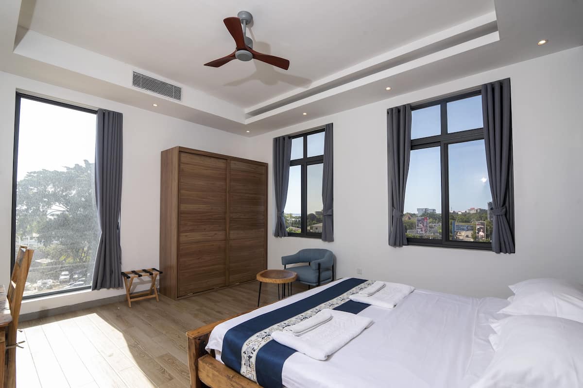 Een moderne hotelkamer met een groot bed, een plafondventilator, stadszicht en een houten garderobe.