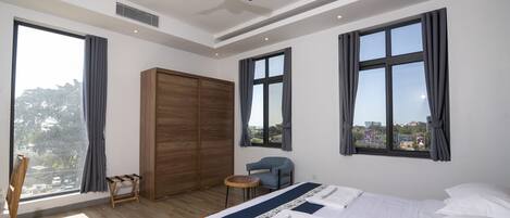 Moderni hotellihuone, jossa on suuri sänky, kattotuuletin, näkymä kaupunkiin ja puinen vaatekaappi.