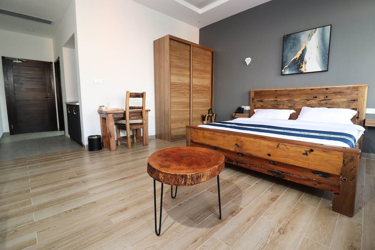 Een slaapkamer met een houten bed, een rond houten tafeltje, een houten kast en een stoel.