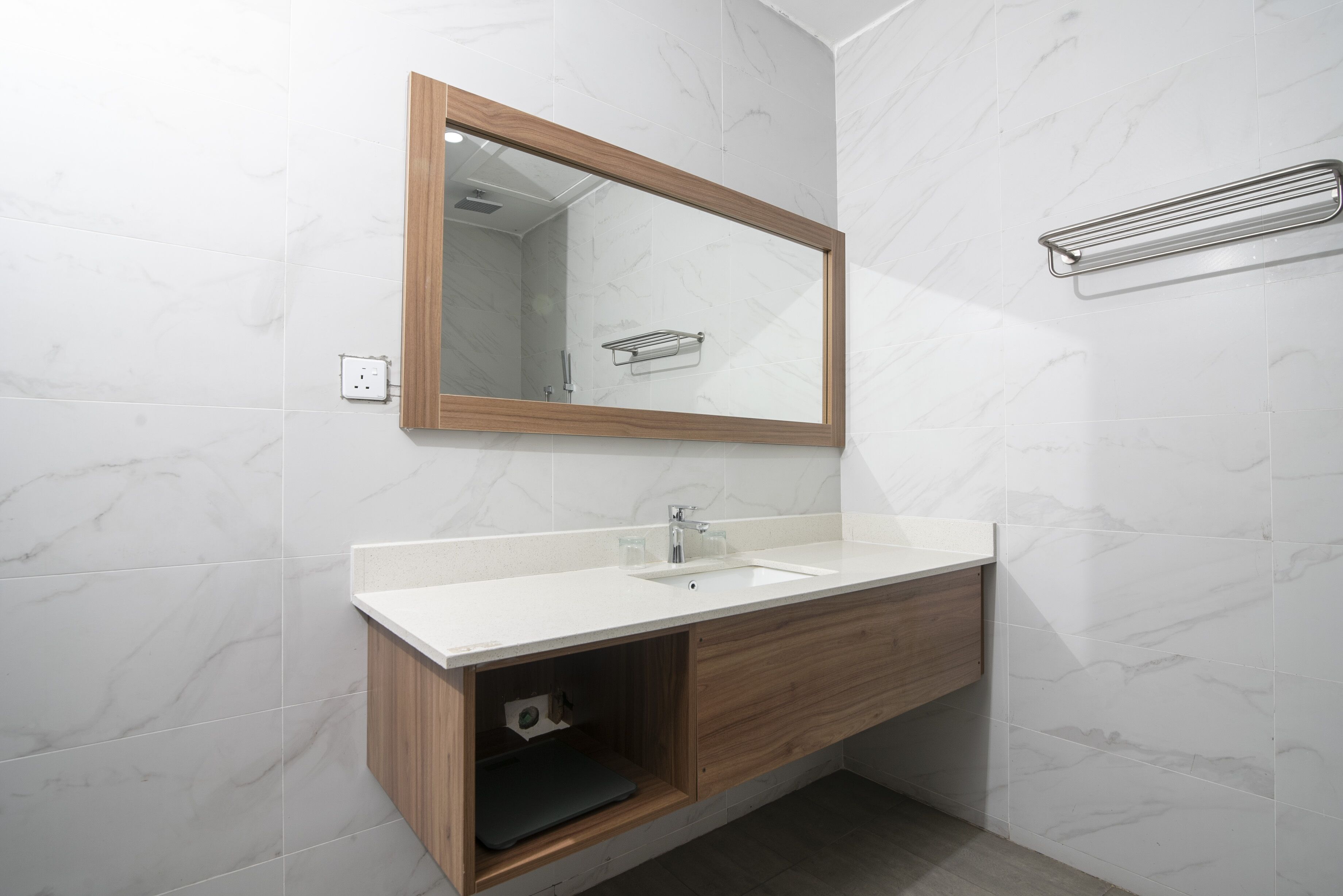 A modern bathroom with a wooden vanity, a large mirror, and a towel rack.