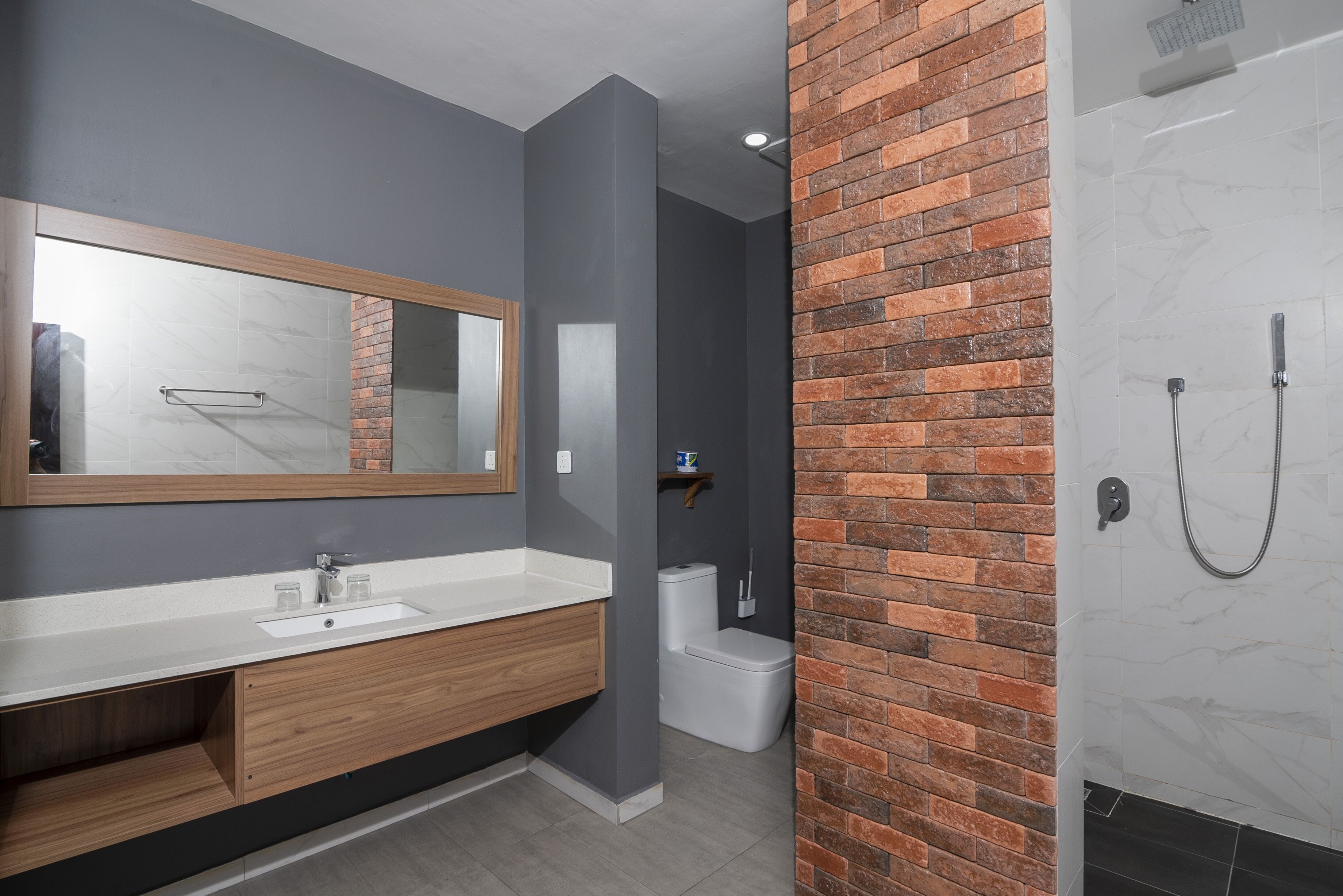Un baño moderno con tocador de madera, un espejo grande y zona de ducha con revestimiento de ladrillo.