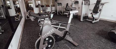 Une salle de sport équipée de vélos d’exercice, d’appareils de musculation et d’un mur recouvert de miroirs.