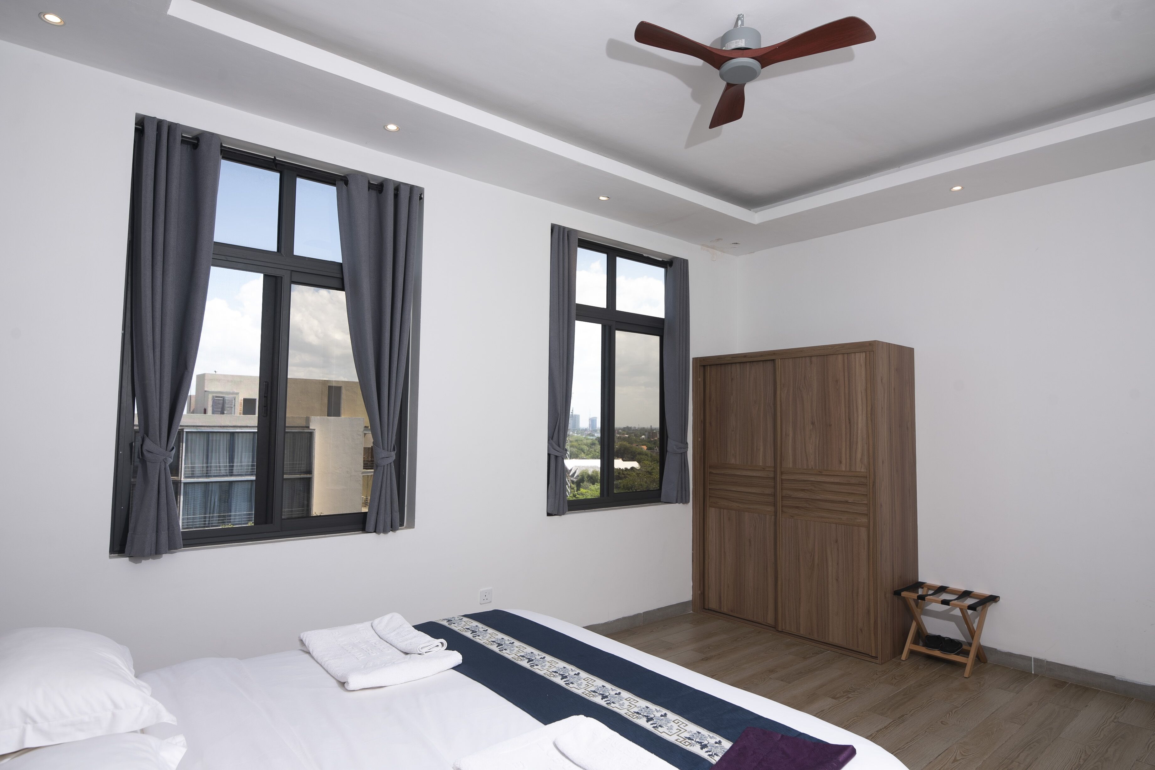 A bedroom with a bed, two windows, a ceiling fan, and a wardrobe.