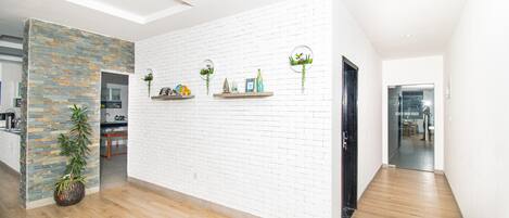A modern interior with a white brick wall, wooden flooring, and a kitchen area visible through an open doorway.