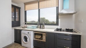 Een moderne keuken met een ingebouwde wasmachine, oven en een groot raam met zonwering.