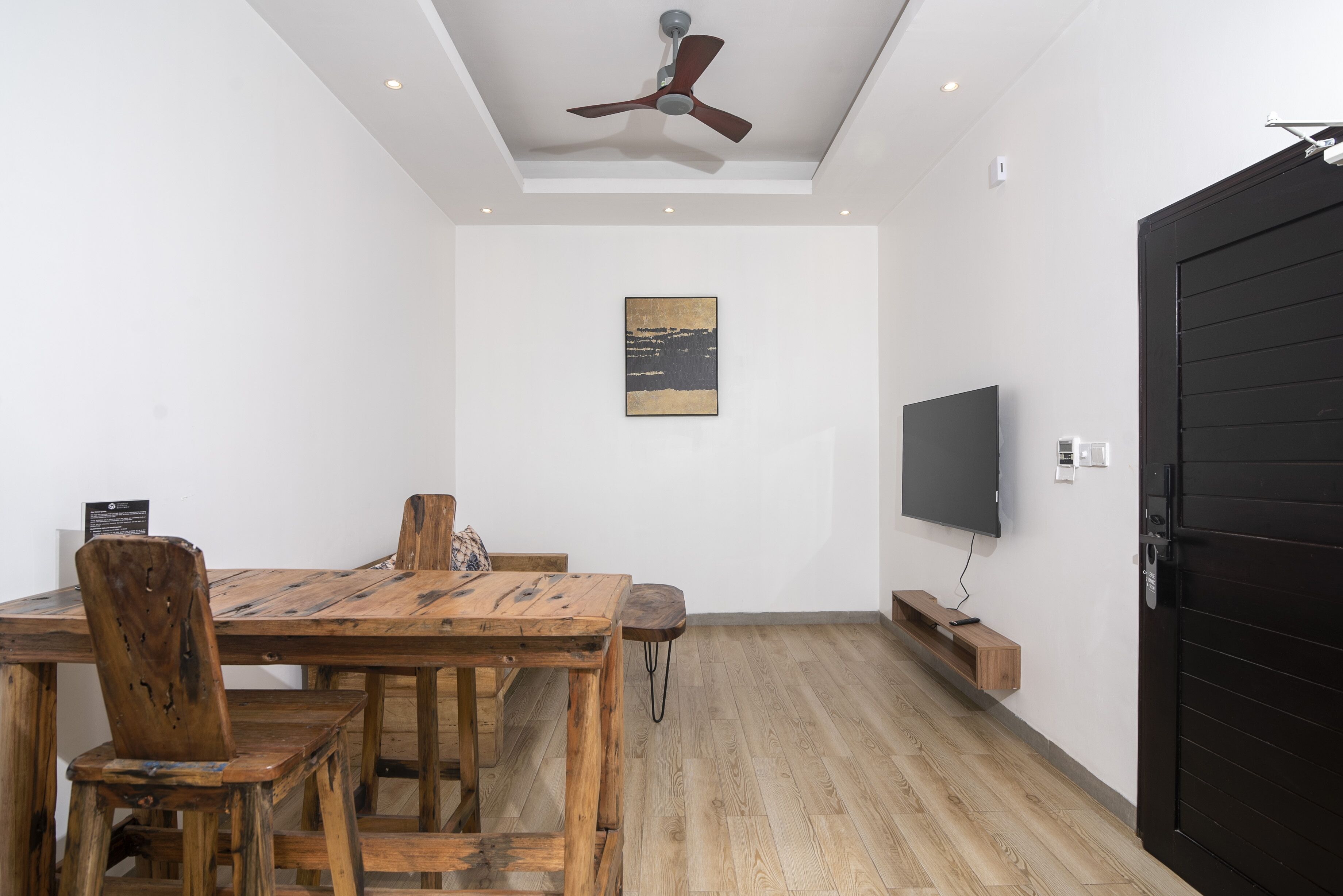 A dining area with a wooden table and chairs, a ceiling fan, a mounted TV, and a black door.