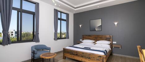 A modern bedroom with a wooden bed, a blue chair, a round wooden table, and large windows with curtains.