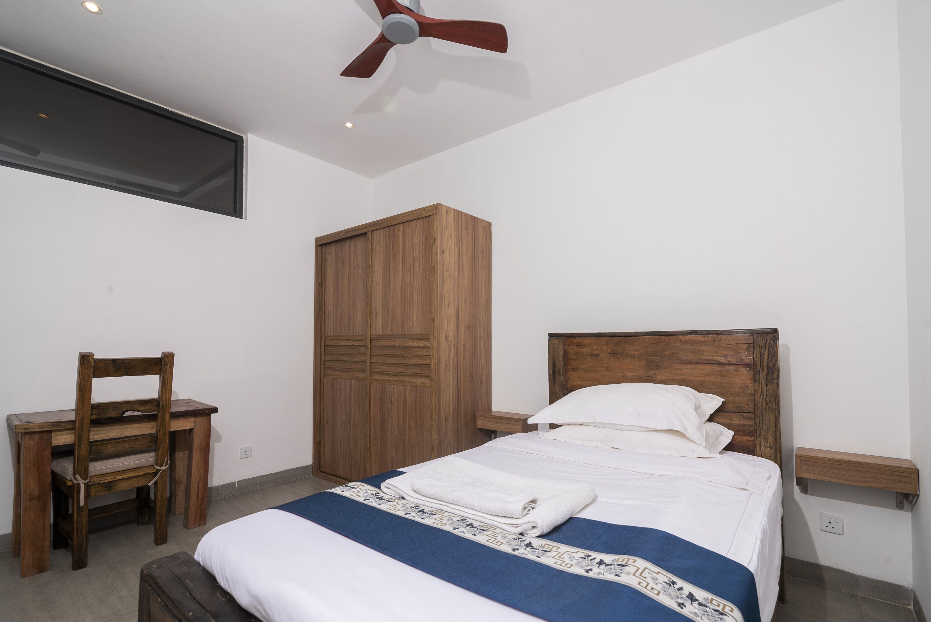 Un dormitorio con cama, un armario de madera, un escritorio con silla y un ventilador de techo.