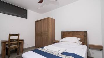 Un dormitorio con cama, un armario de madera, un escritorio con silla y un ventilador de techo.
