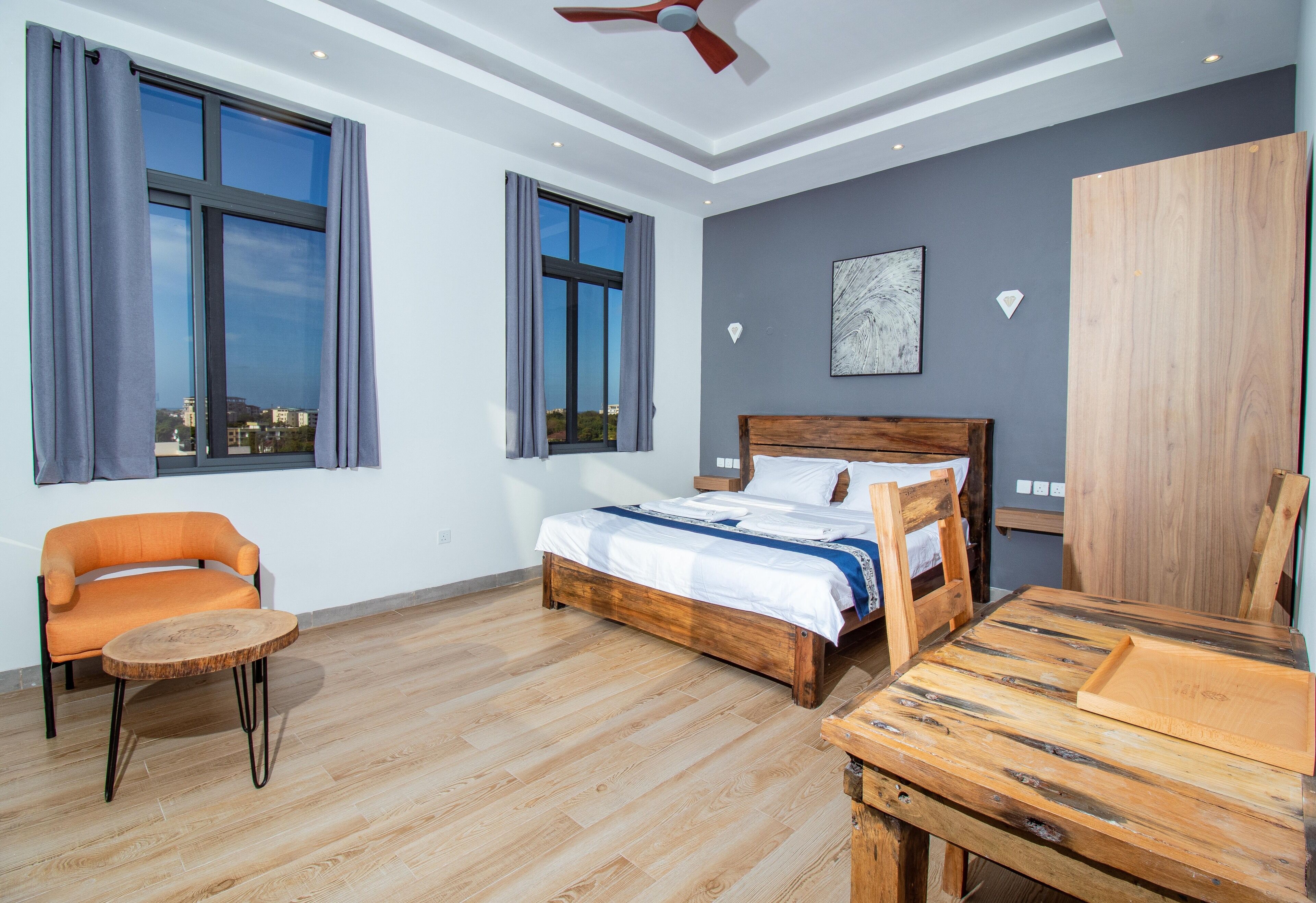 Une chambre à coucher moderne avec un lit en bois, une table ronde en bois, un canapé et de grandes fenêtres avec des rideaux.