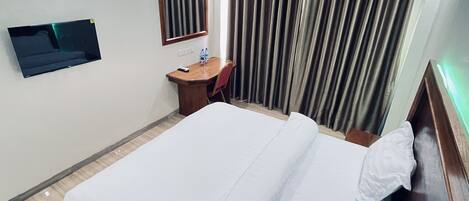 Una habitación de hotel con una cama grande, un escritorio con silla, un televisor de pantalla plana en la pared y una ventana con cortinas.