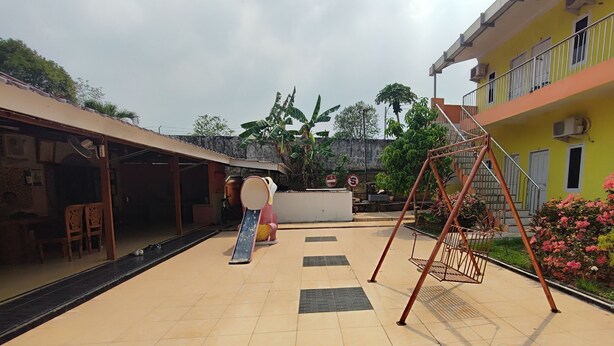 A courtyard with a swing set, a slide, and a staircase leading to a balcony. - Hotel O Garuda Bandara Guesthouse (Palembang)