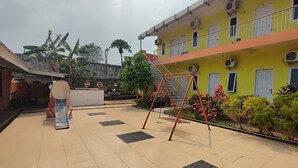 A courtyard with a playground, a yellow building with balconies, and a garden with various plants. - Hotel O Garuda Bandara Guesthouse (Palembang)