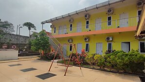 A multi-story yellow building with balconies, air conditioning units, and a swing set in the courtyard. - Hotel O Garuda Bandara Guesthouse (Palembang)
