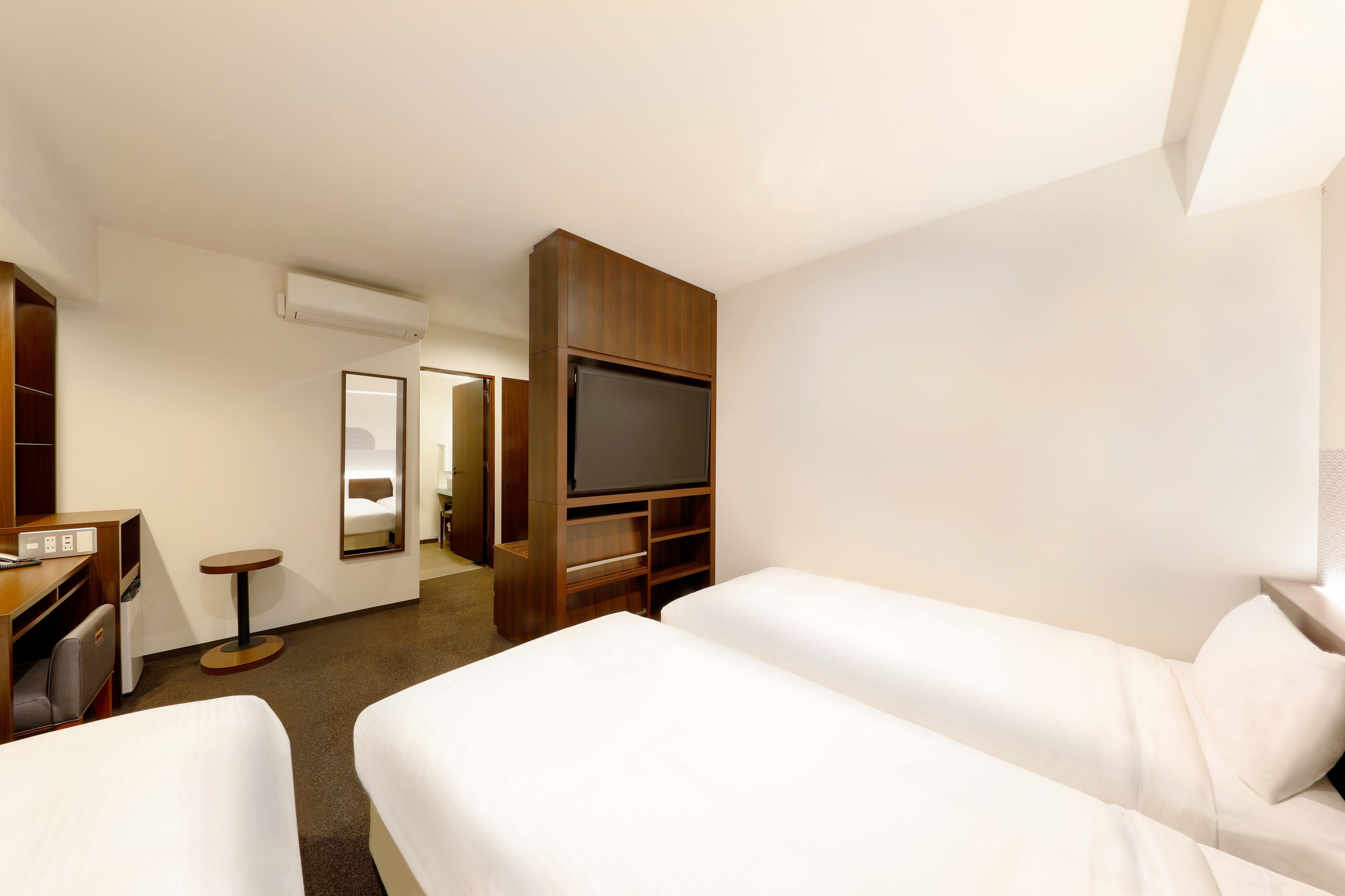 A hotel room with two beds, a desk, a TV, and a mirror.