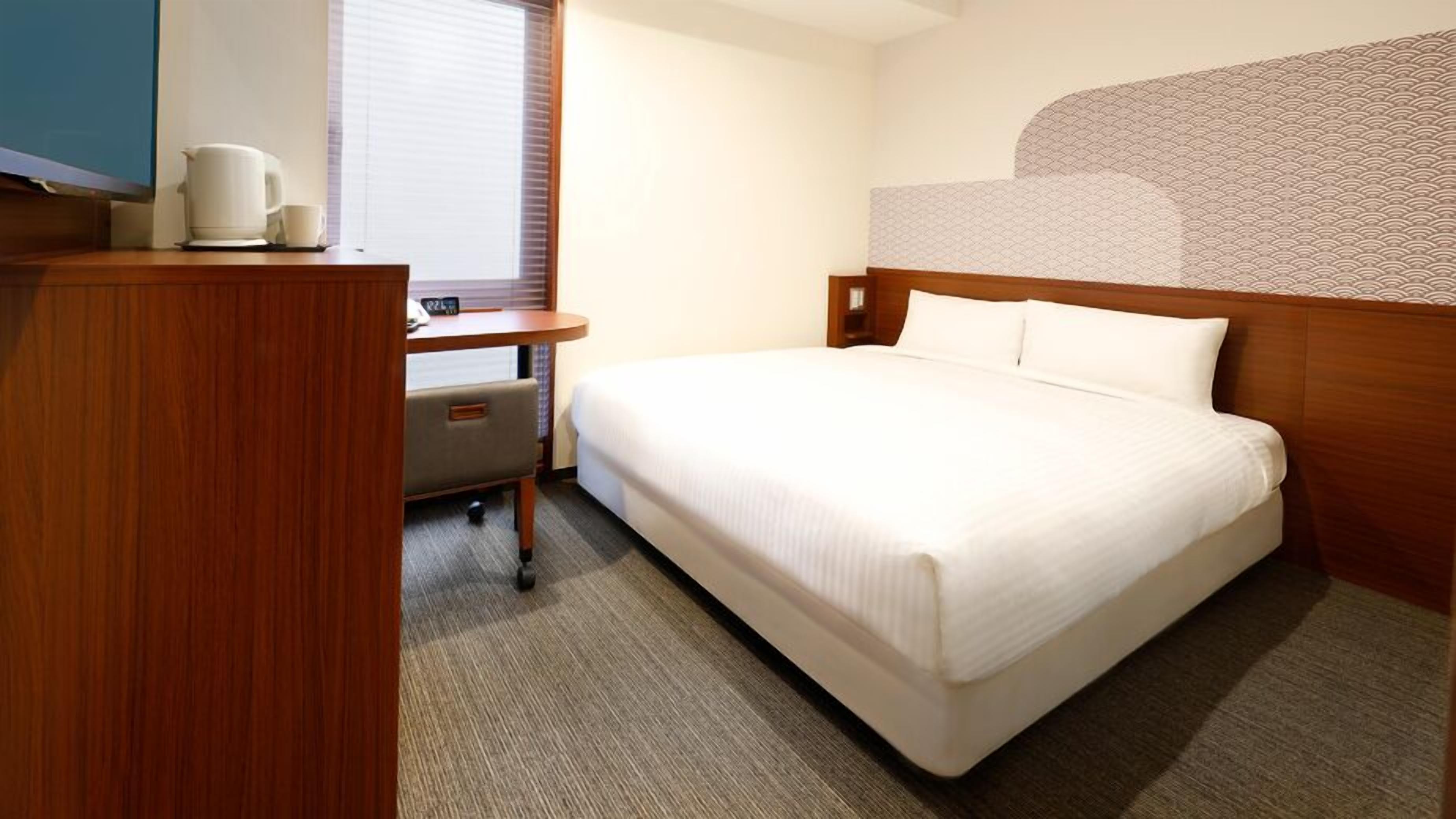 A hotel room with a bed, a desk with a chair, a coffee maker, and a TV.