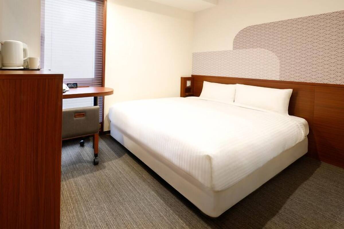 A hotel room with a bed, a desk with a chair, a coffee maker, and a TV.