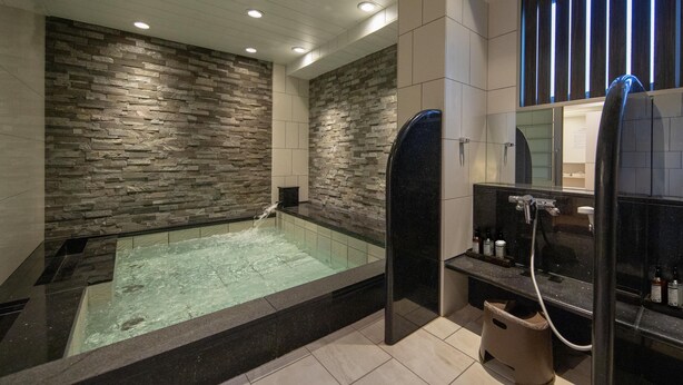 A modern bathroom with a stone wall, a glass-enclosed jacuzzi, and a black vanity with a mirror. - Hop Inn Kyoto Shijo Omiya (Kyoto)