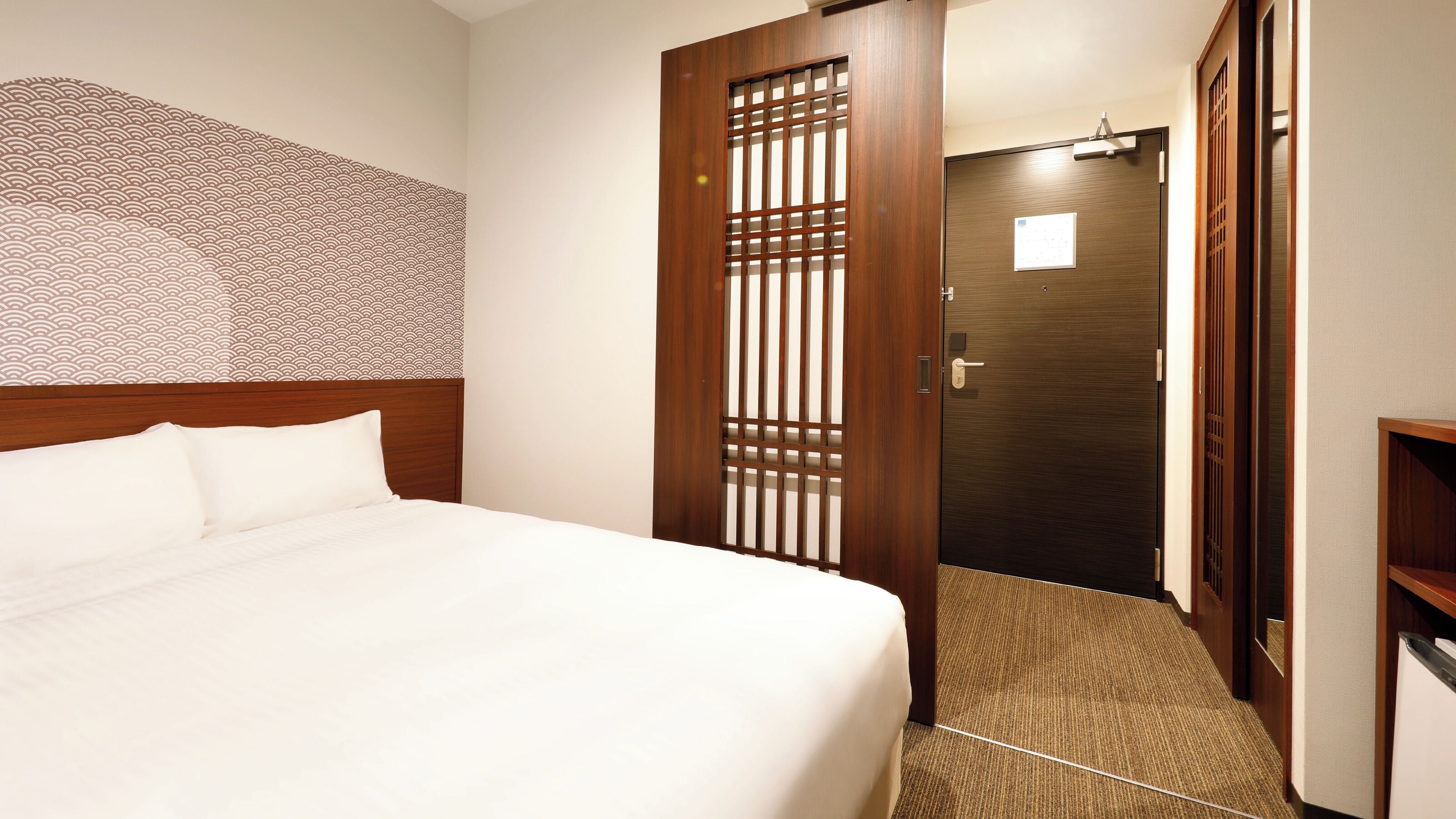 A hotel room with a bed, a wooden door, and a patterned wall.