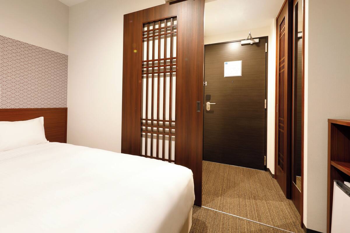 A hotel room with a bed, a wooden door, and a patterned wall.