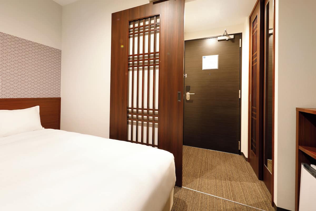 A hotel room with a bed, a wooden door, and a patterned wall.