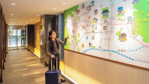 A person pointing at a wall map in a hallway with a suitcase. - Hop Inn Kyoto Shijo Omiya (Kyoto)