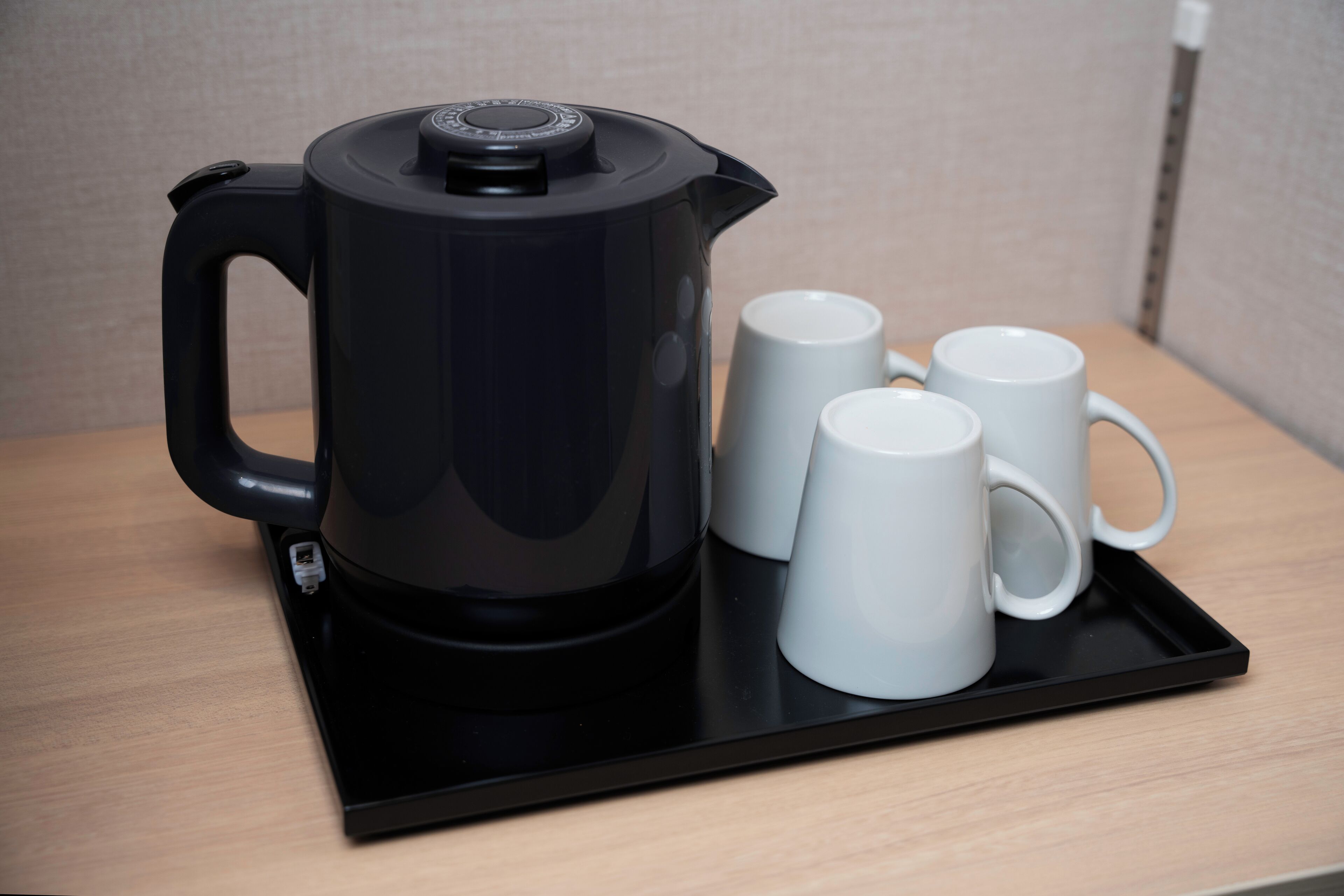 Una tetera eléctrica negra sobre una bandeja con dos tazas blancas.