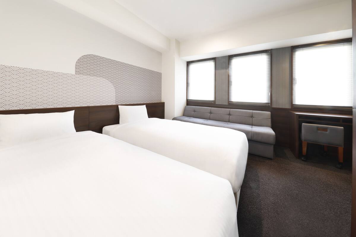 A hotel room with two beds, a seating area, and large windows.