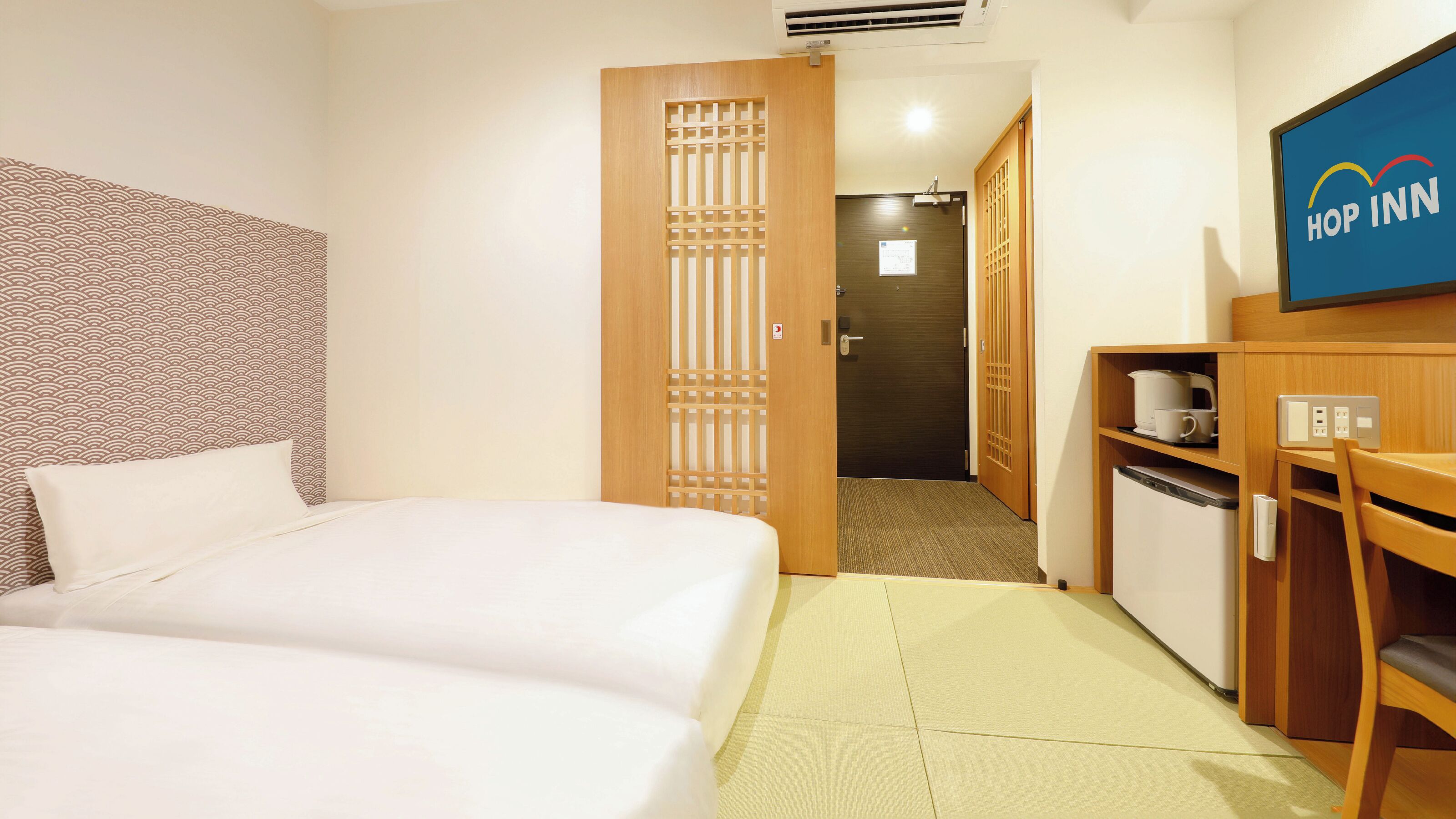 A hotel room with a bed, a desk with a computer, a microwave, and a television displaying the hotel name.