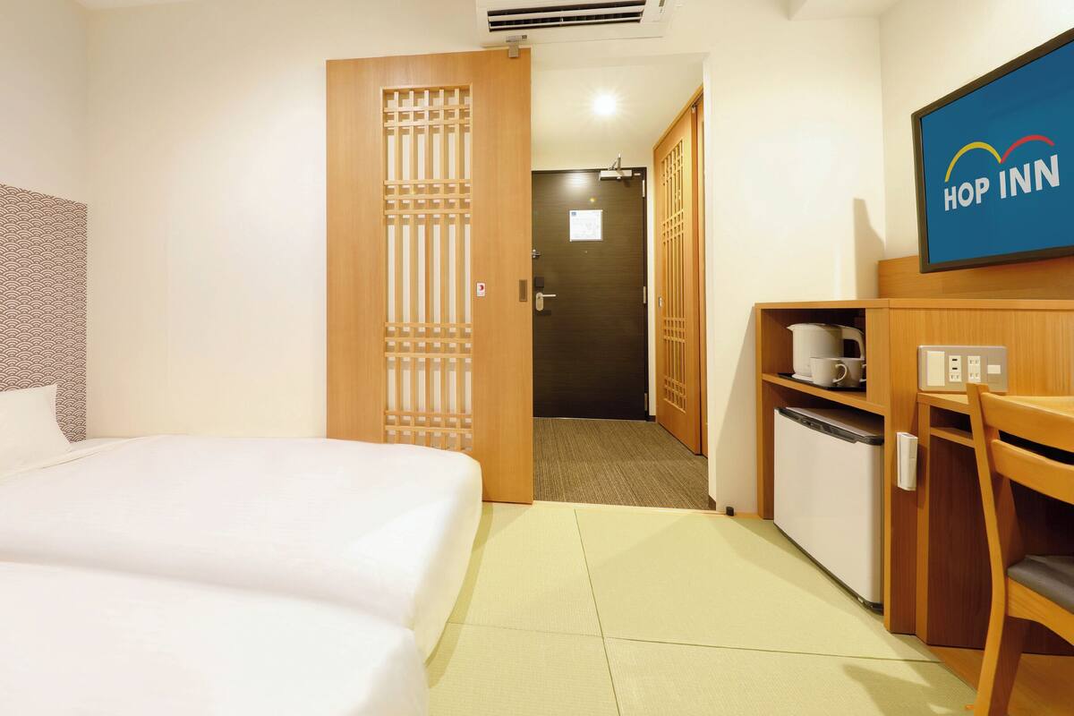 A hotel room with a bed, a desk with a computer, a microwave, and a television displaying the hotel name.