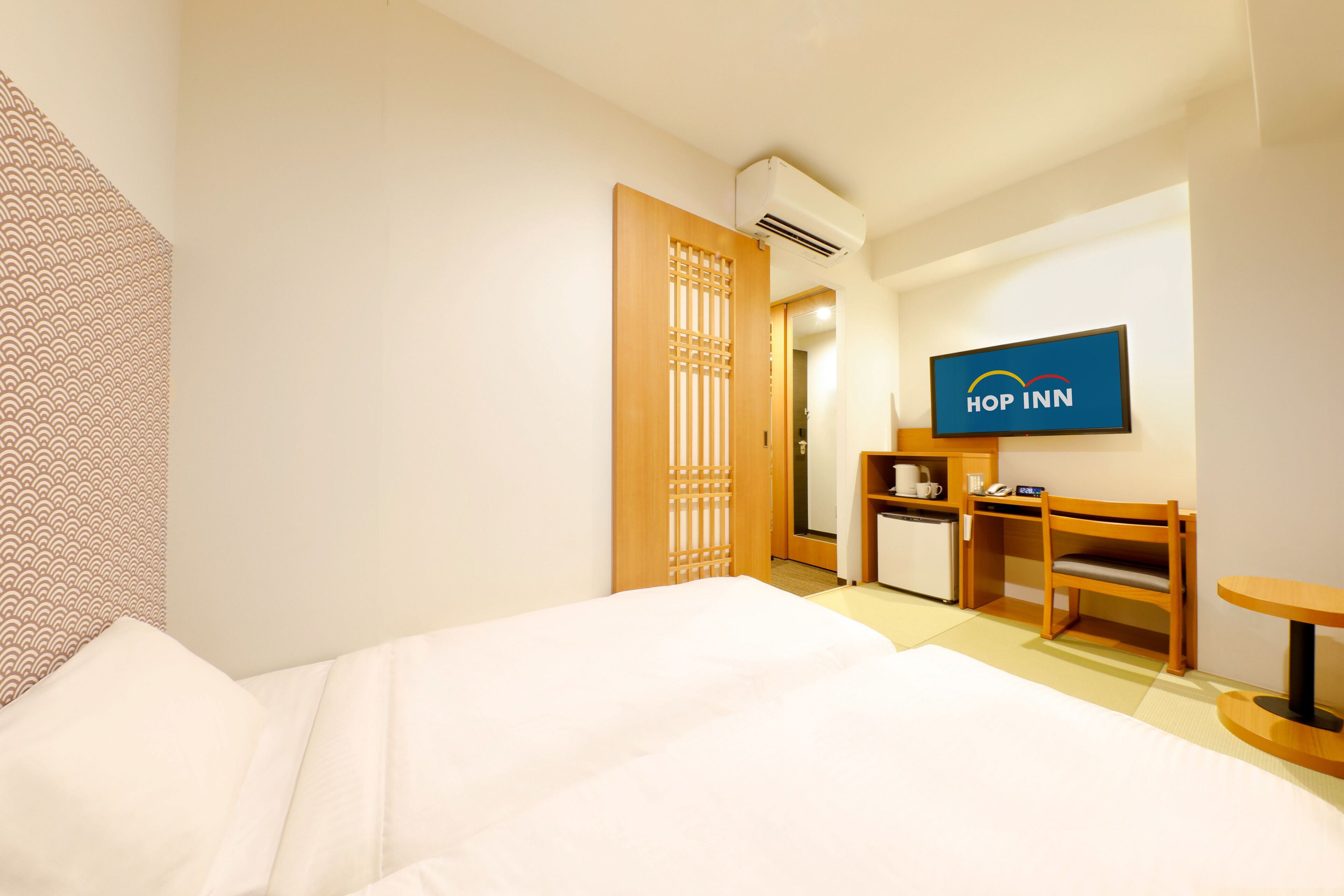 A hotel room with a bed, a desk, a chair, a television, and a small kitchenette.