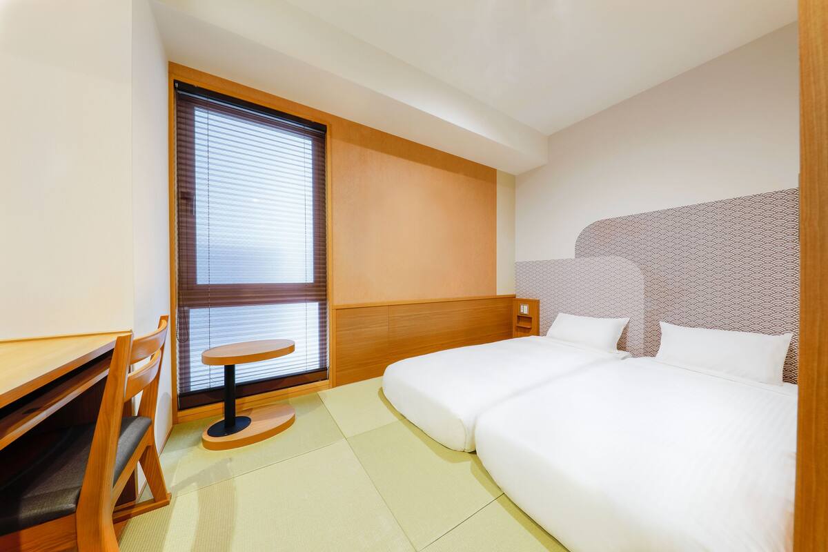A hotel room with a bed, a desk, and a window with blinds.