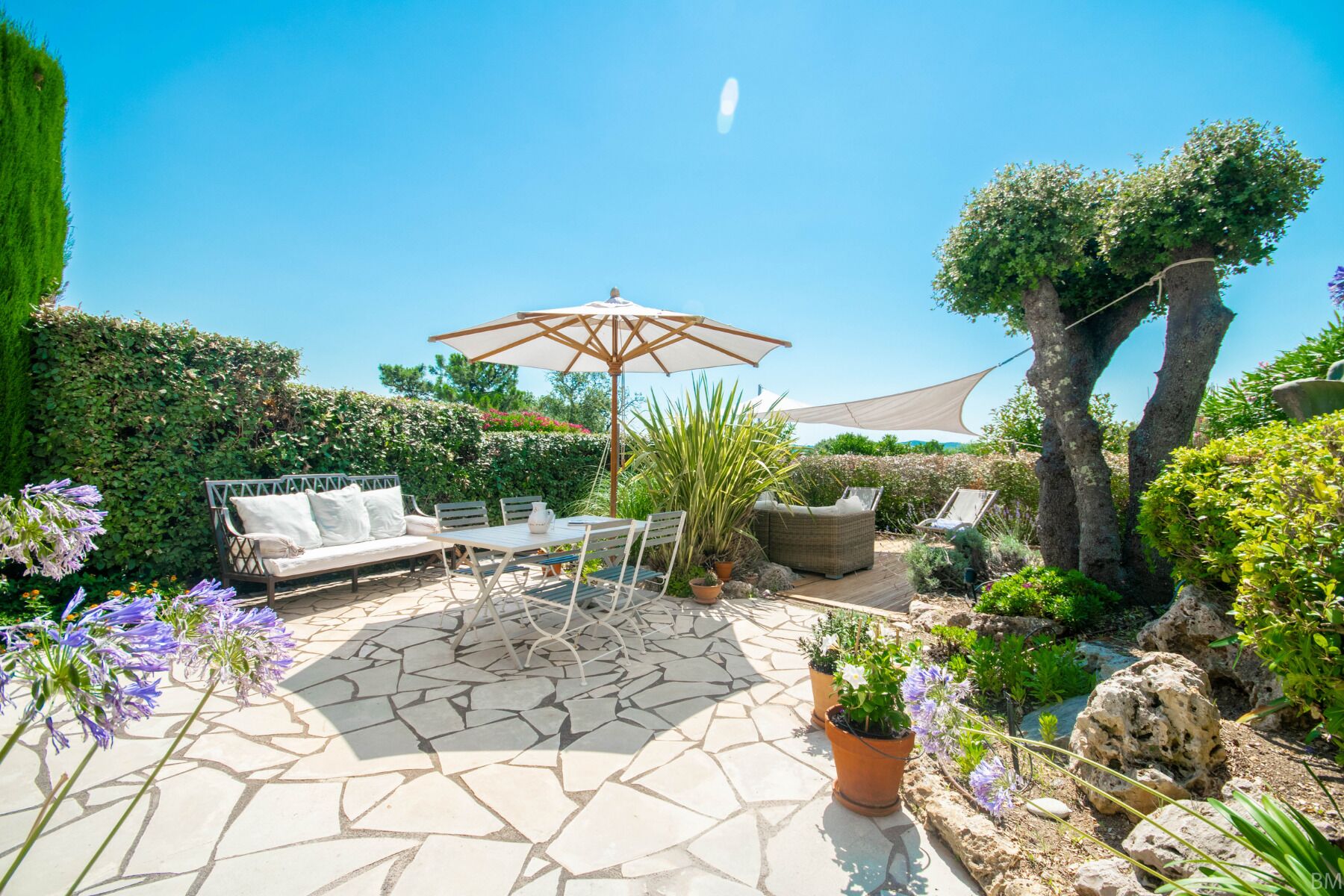 An outdoor patio with a stone floor, a white sofa, a dining table, and a large umbrella.