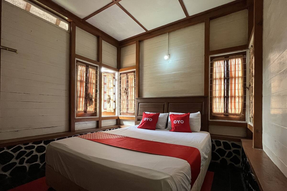 A bedroom with a bed, a red throw blanket, and a headboard.