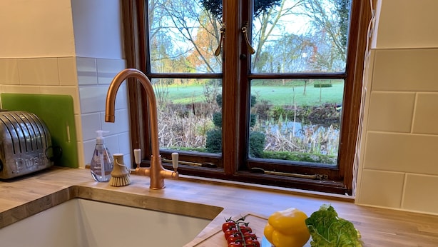 A kitchen with a sink, a green chair, a Dualit toaster, a copper faucet, a bottle of dish soap, a cutting board with tomatoes, a yellow bell pepper, and a head of lettuce.
