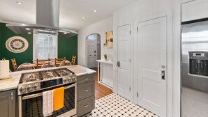 Une cuisine moderne équipée d’une cuisinière à gaz, d’un four et d’une hotte en acier inoxydable. On y trouve une table à manger avec des chaises et une horloge au mur.