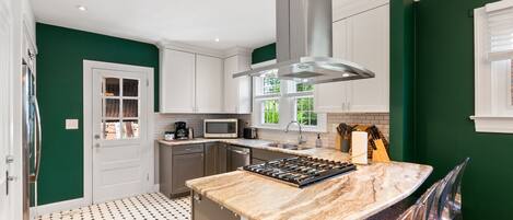 A modern kitchen with white cabinets, a stainless steel range hood, a marble countertop, and a patterned floor.
