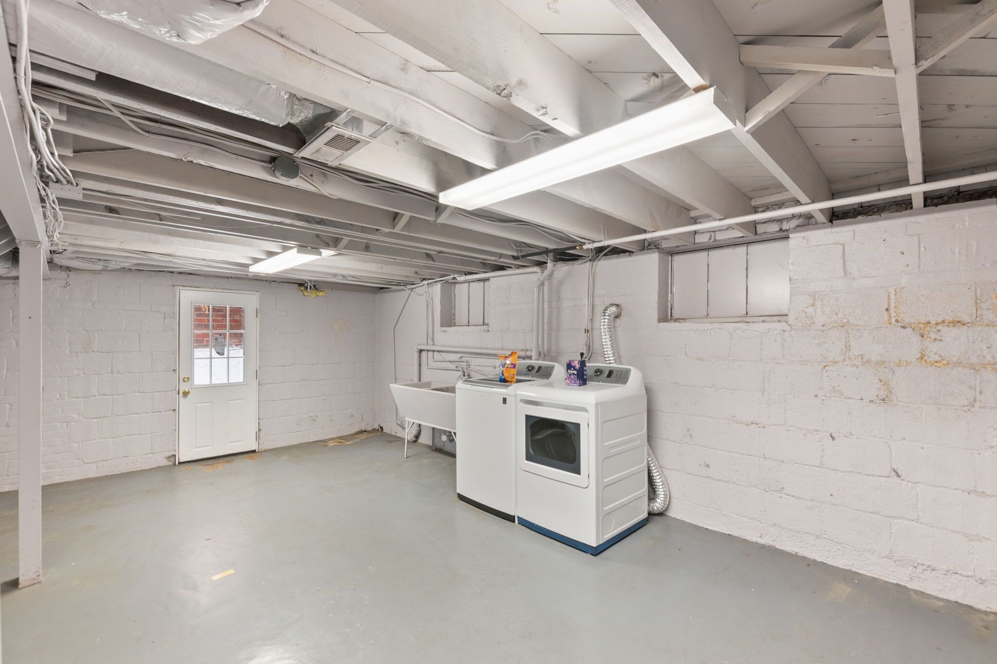 Un cuarto de lavandería con techo estilo industrial, paredes de ladrillo blanco y una lavadora grande.
