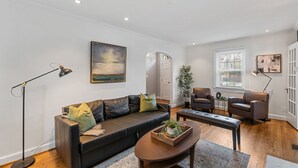 Un salon moderne avec un canapé en cuir noir, deux fauteuils, une table basse et un tableau accroché au mur.