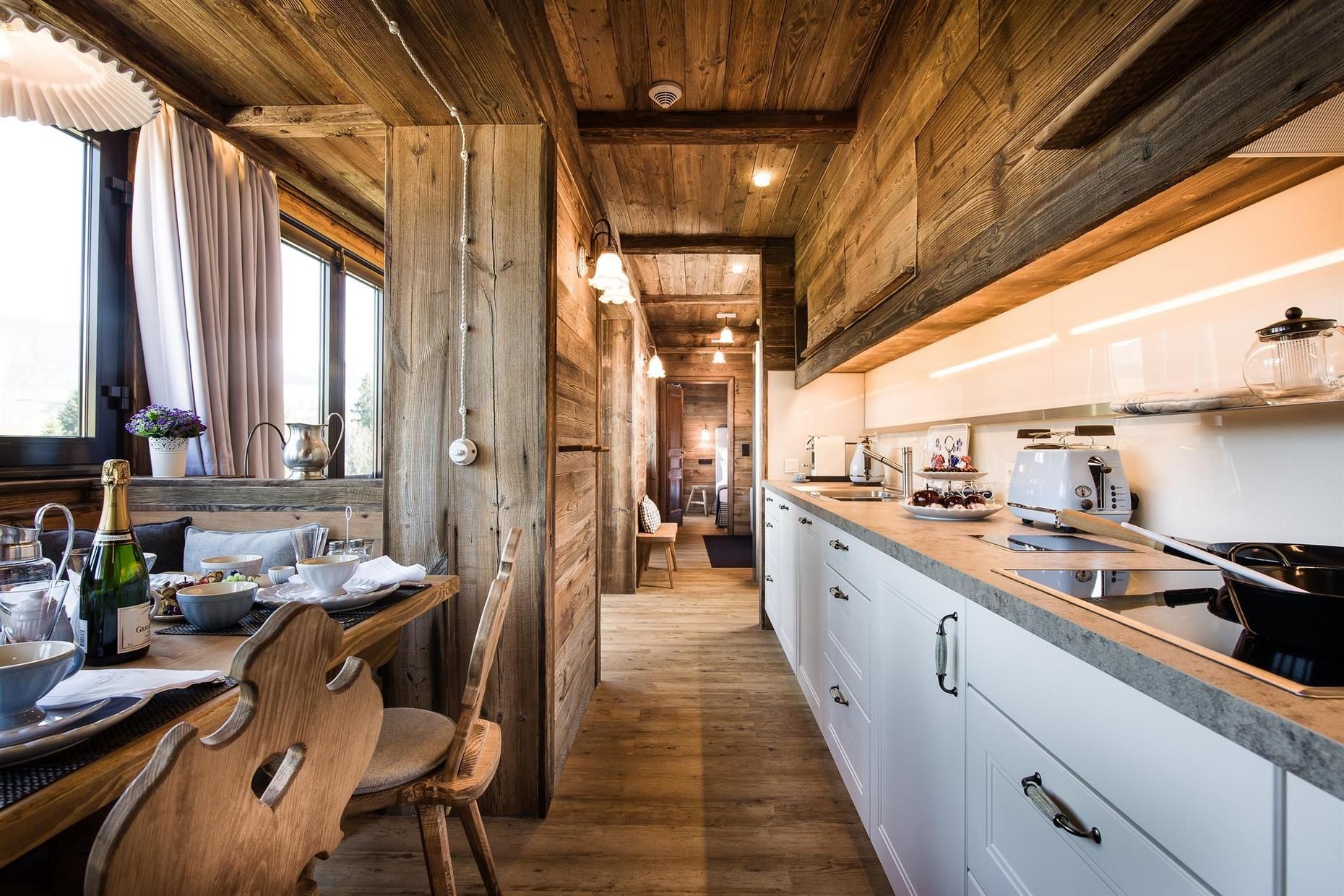 A wooden interior with a kitchen area, wooden dining table, and chairs.