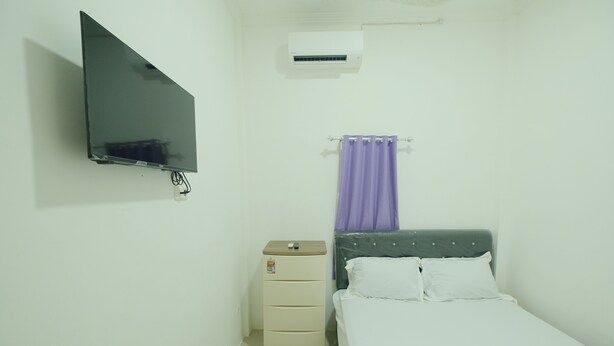 A small, clean room with a bed, a TV mounted on the wall, a small cabinet, and a window with a purple curtain. - Hotel O Penginapan Permata Hijau Syariah Near Bukit Teletubbies (Parepare)