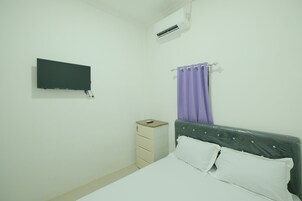 Un dormitorio con cama, mesita de noche, televisor montado en la pared y cortina púrpura.