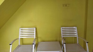 Two white chairs with slatted backs and metal frames, positioned against a yellow wall in a corner. - Hotel O Penginapan Permata Hijau Syariah Near Bukit Teletubbies (Parepare)