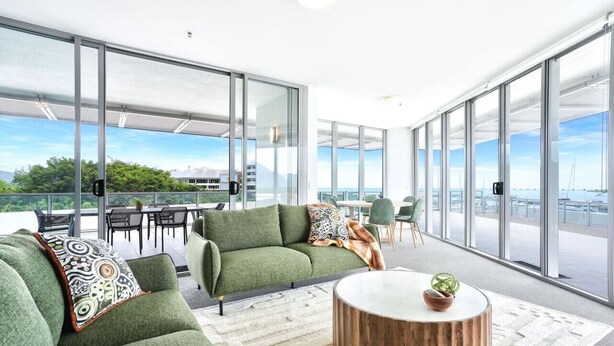 Un espace de vie moderne avec un canapé vert, une table basse ronde et une vue sur le paysage urbain grâce à de grandes fenêtres en verre.
